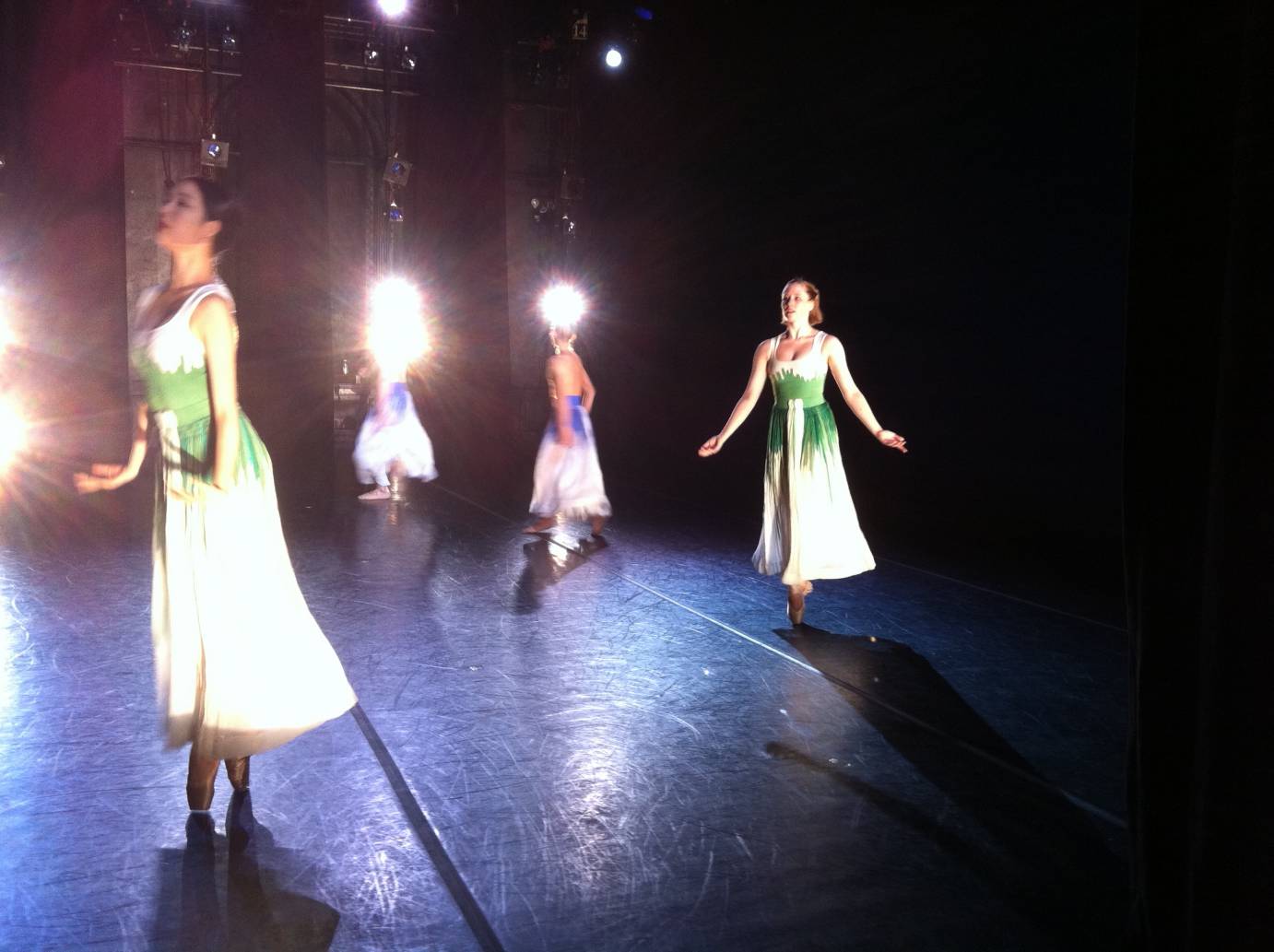 Carissa Landes, in a floaty green and white dress, extends her arms in a low V in a piece by Mark Morris