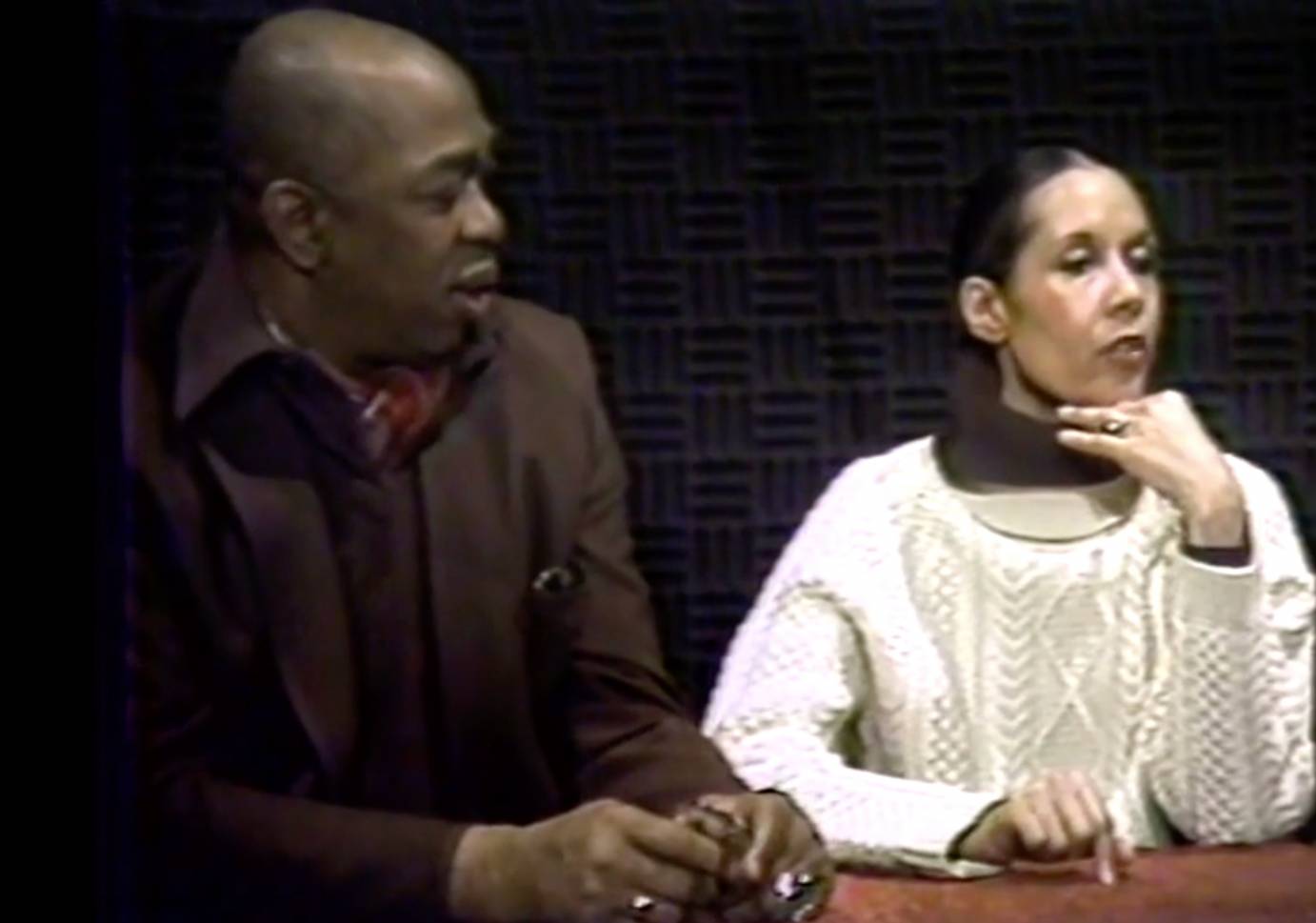 a legendary team Geofferey Holder, a dark colored, man in a brown suit, with a mulitcolored ascot, and Carmen De Lavallade his wife, a carmel colored woman with black hair tied back in a ponytail, wearing a brown turtle-neck under a white woolen sweater, chat