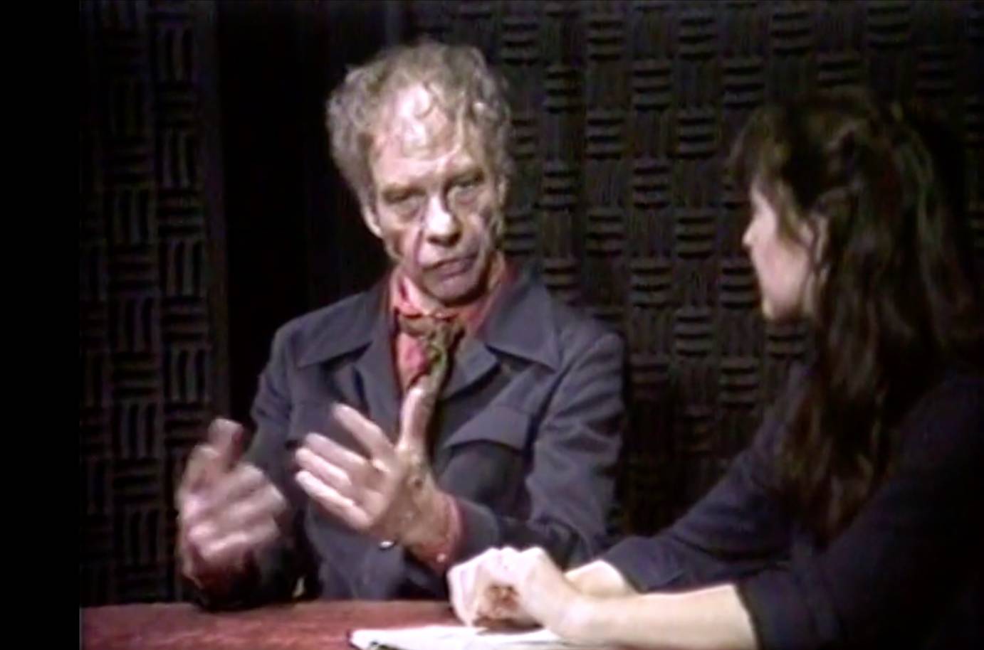 Merce Cunningham white choreographer innovator in purple 1970's style jacket with salmon shirt and a brown scarf is interviewed by a white woman Celia Ipiotis with dark brown hair wearing a purple top