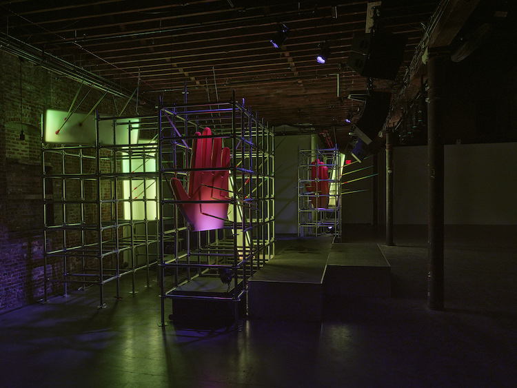 sculptures of oversized pink pierd hands ensconced in cages. these scupltures exist opposite of the Atlas projections