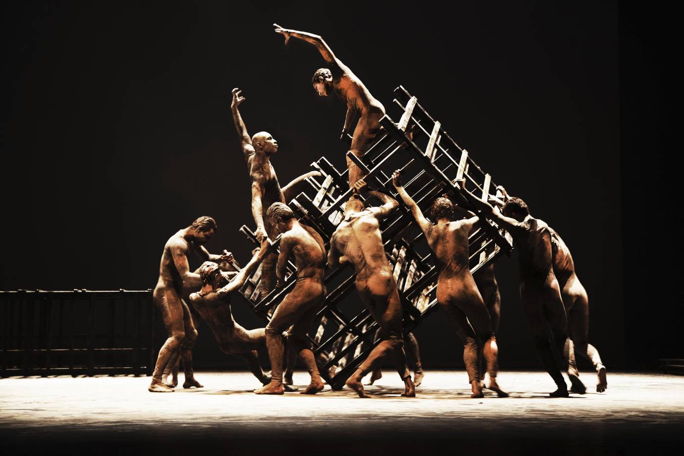 One dancers poses on top of a wooden grid held by other performers