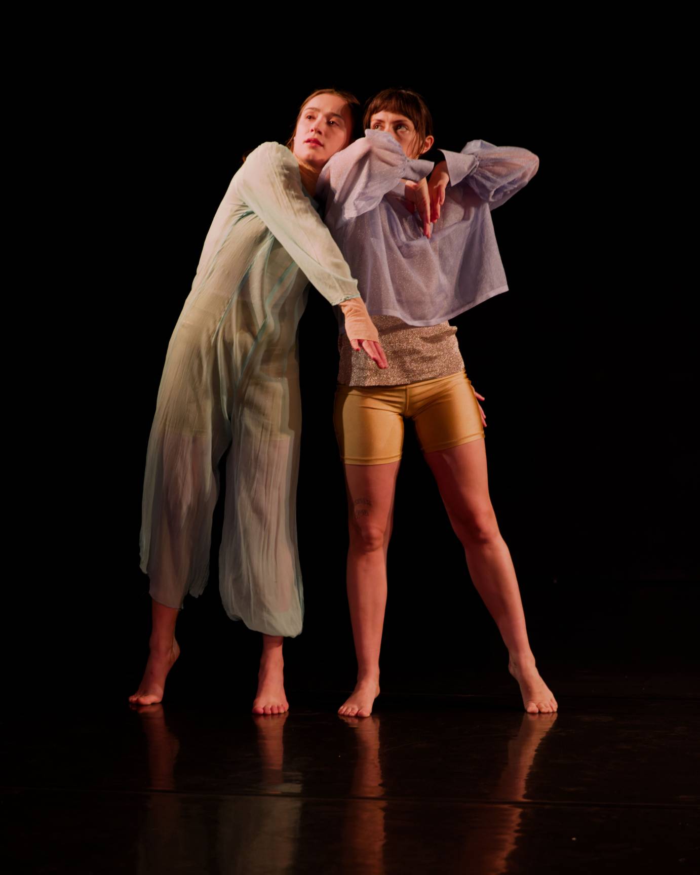 Women in seafoam and lavendar nestle together while standing, their expressions soft and tipped over their right shoulders.