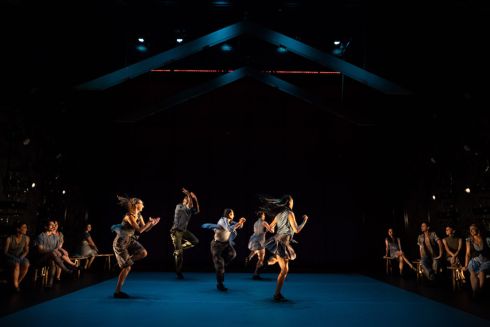 a celebratory sensibility fills this picture as five dancers clap encouraging their friends on the benches to clap  