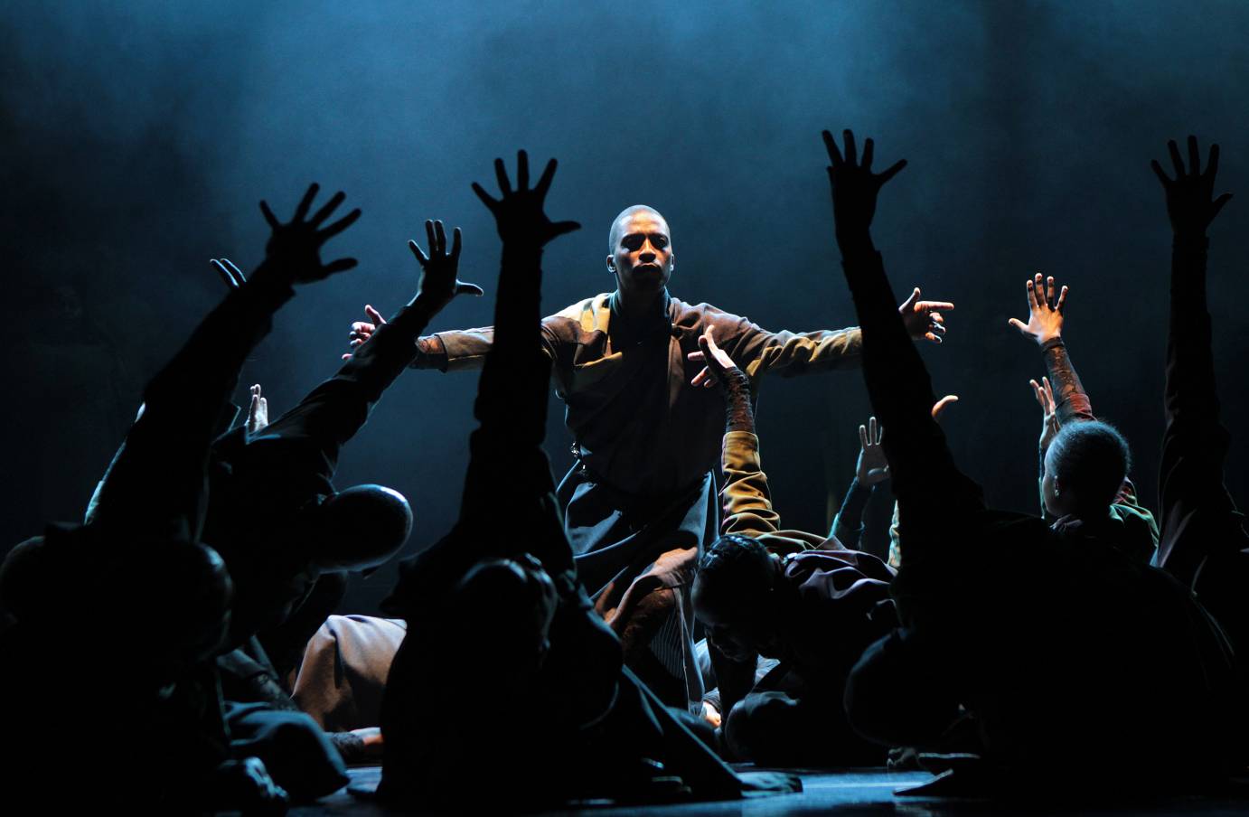 A man kneels in front of a mass of bodies lifting an arm