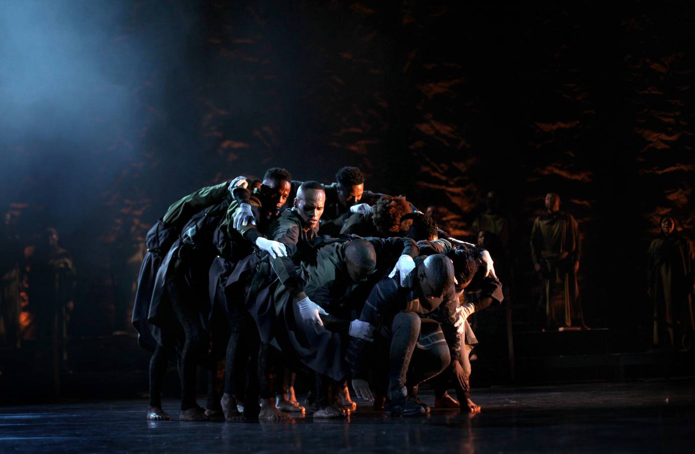 Dancers wearing white gloves form a clump, slumped over each other