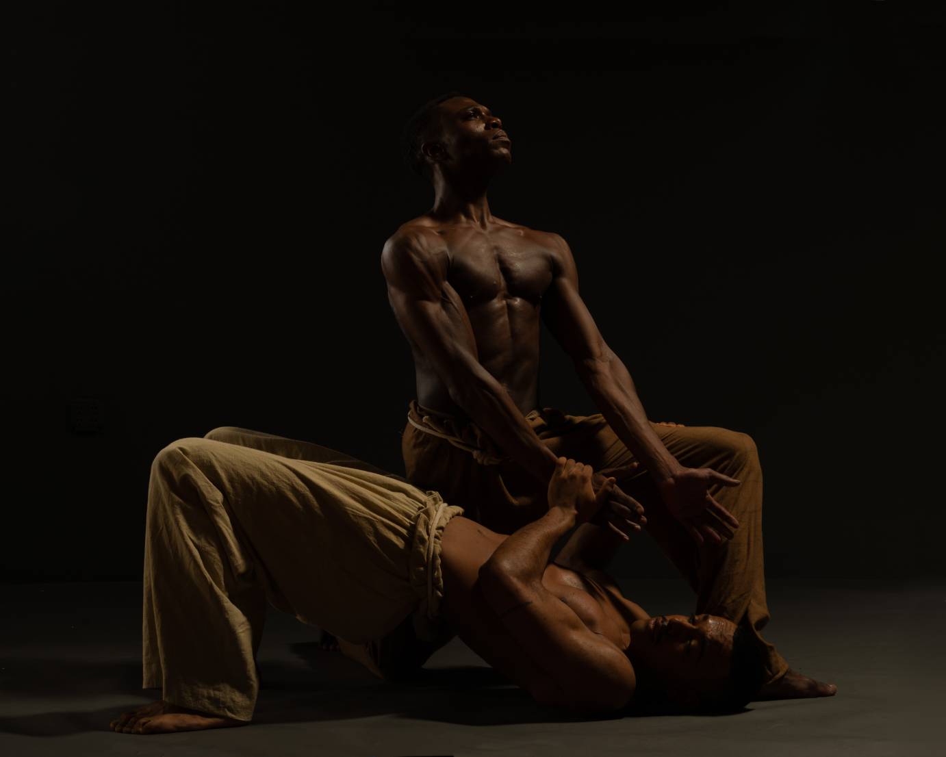 A man kneels, holding another man's hands, who is in a bridge