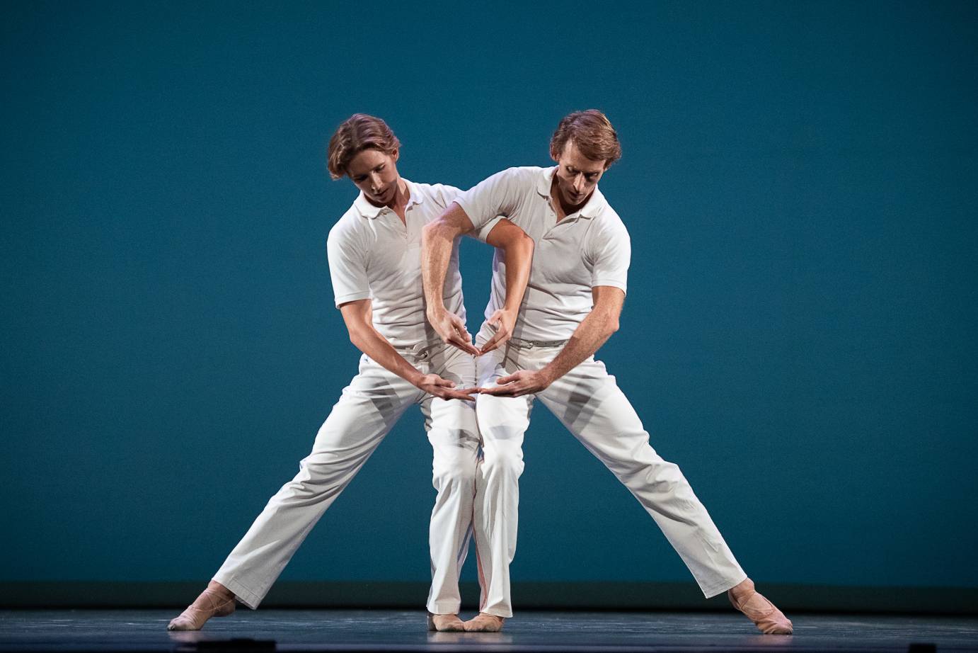 Two men in white polos and pants stand side by side. They loop their arms to form two low ovals
