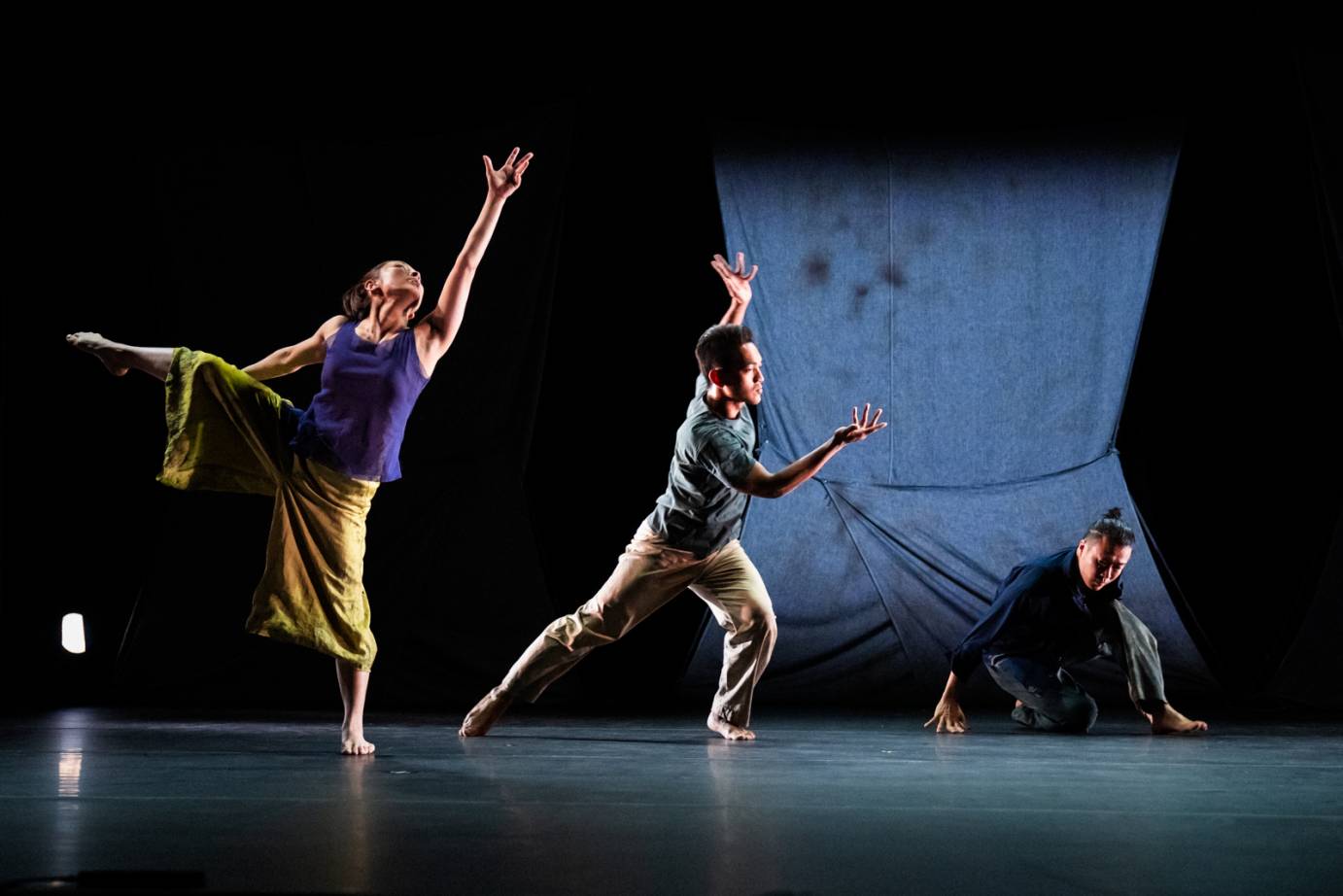 In a diagonal, three dancers gesture emotionally