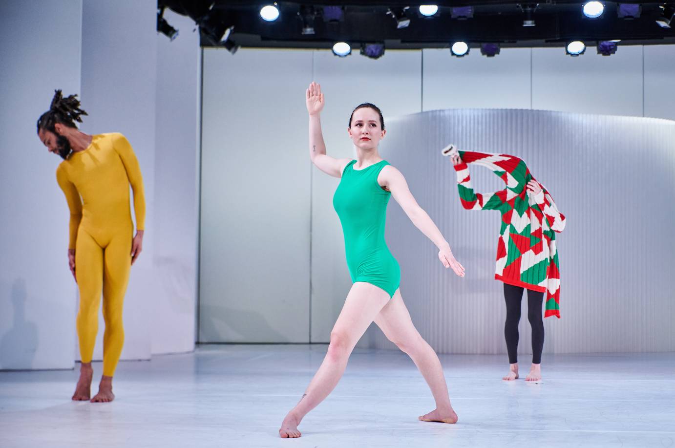 A man with a Christmas sweater stands behind two dancers