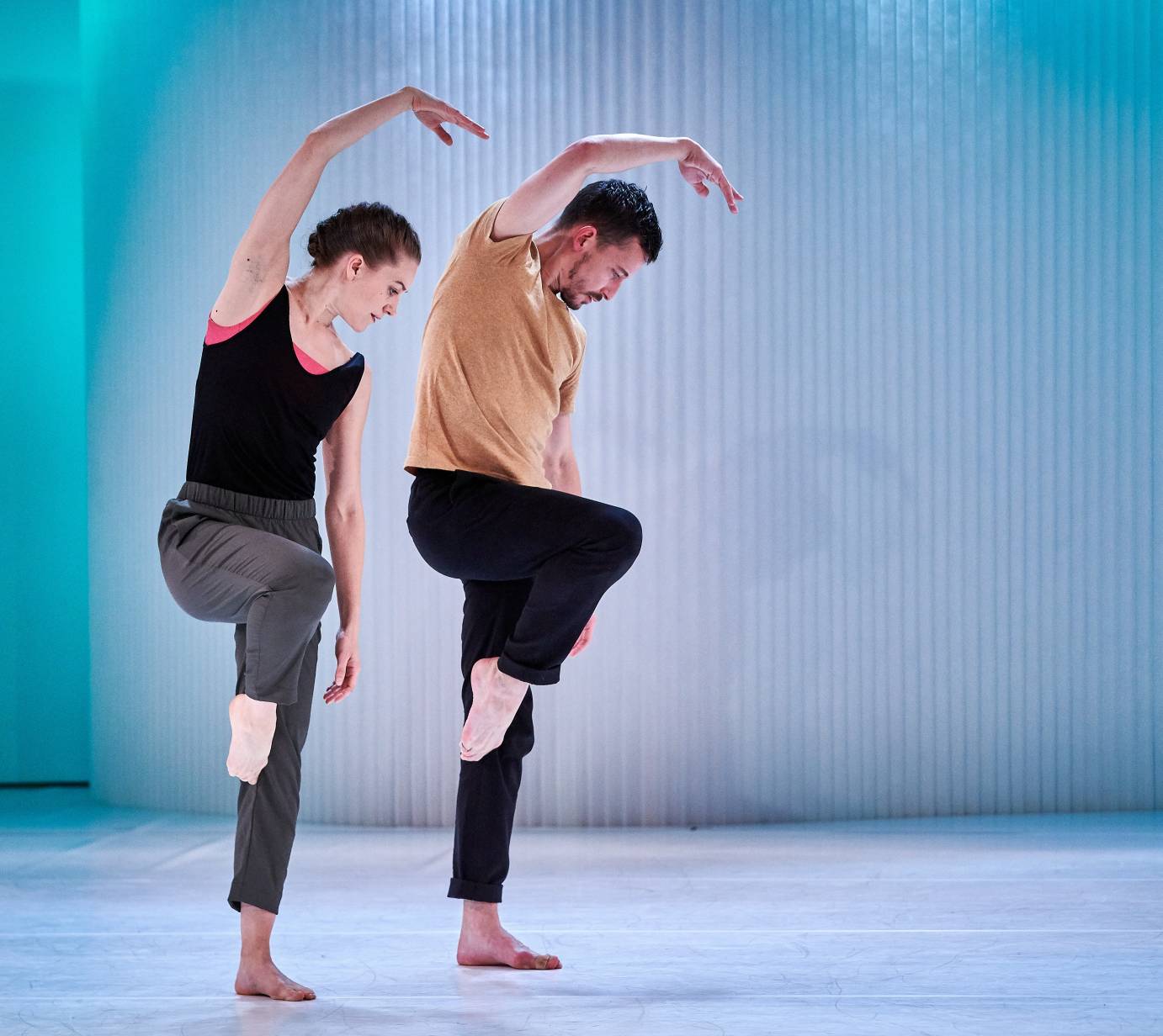 Two dancers in casual clothes curve an arm over their head