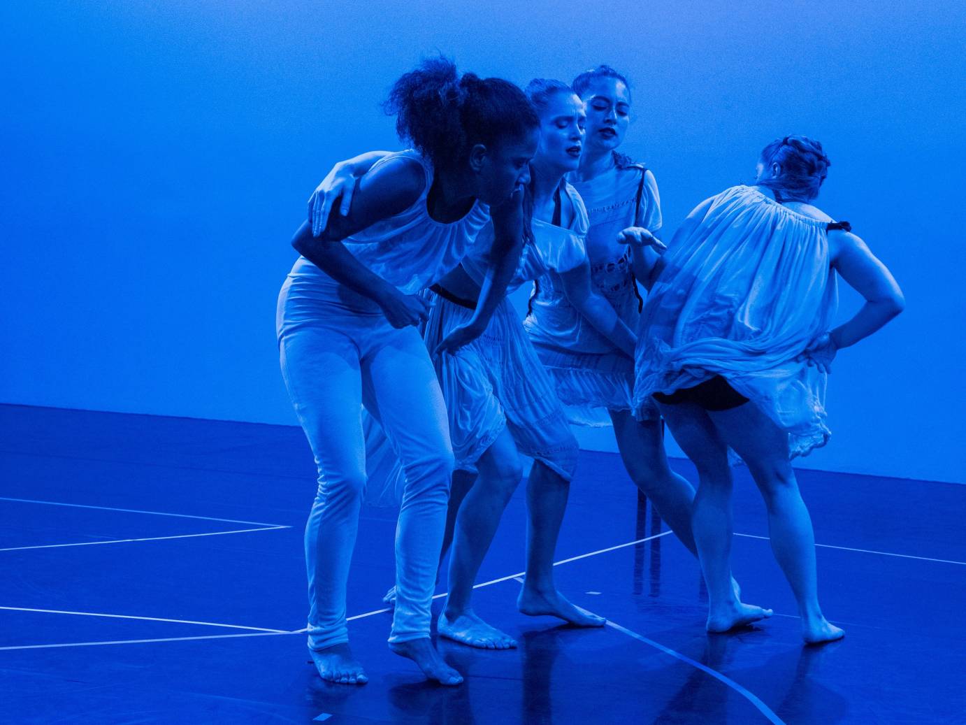 Four women huddle together in blue light