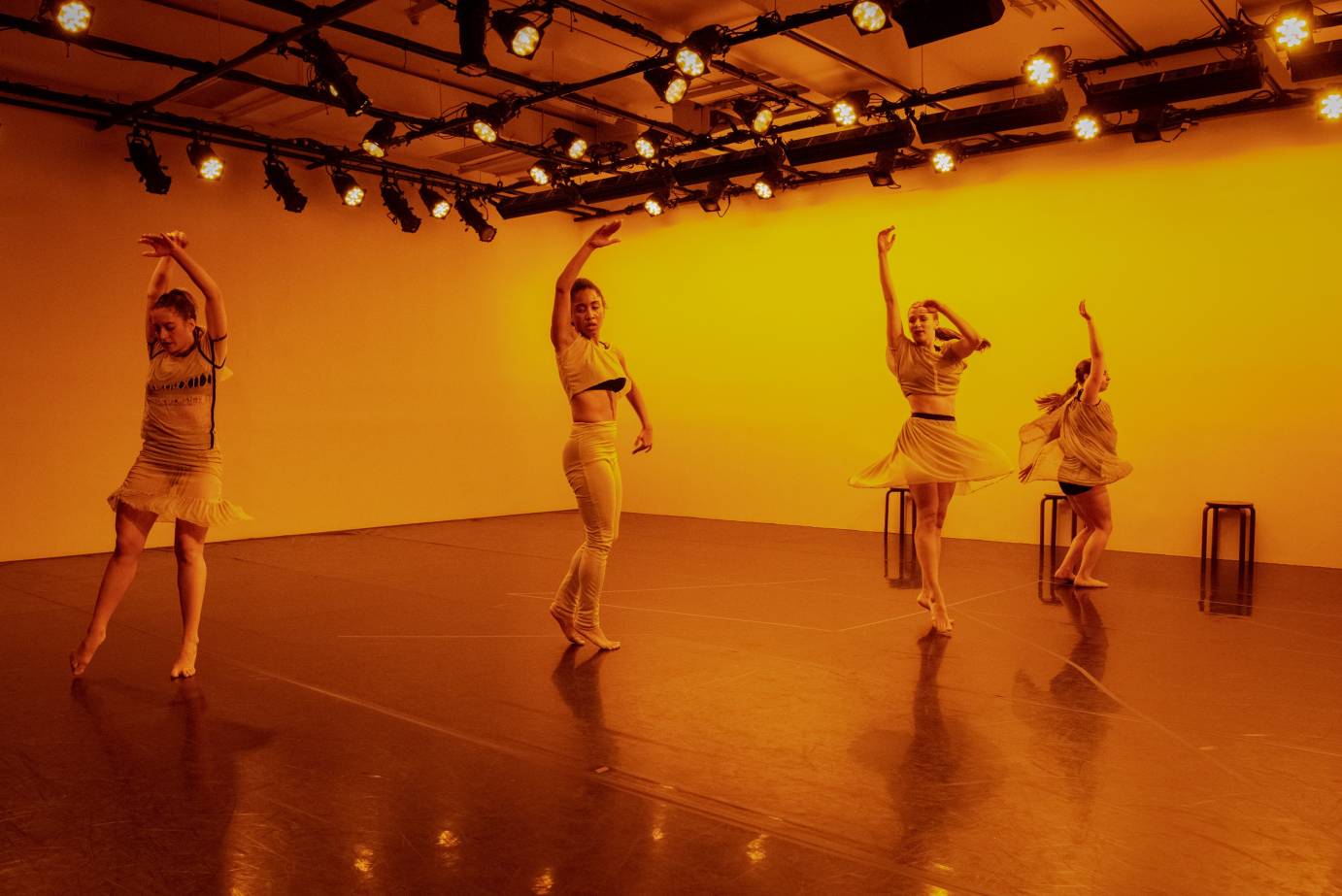 Four women raise an arm as gold light bathes them