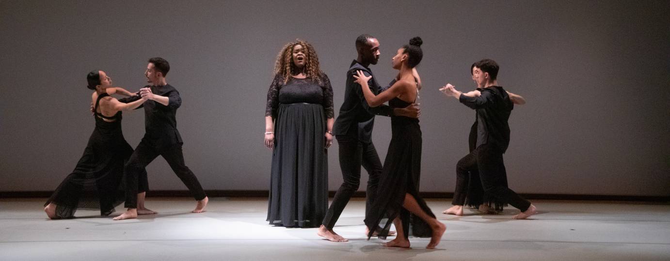 central figure Black woman with long curly light brown hair  dressed in black gown. She is surounded by three couples men and woman of different skin colors also dressed in black evening clothes.