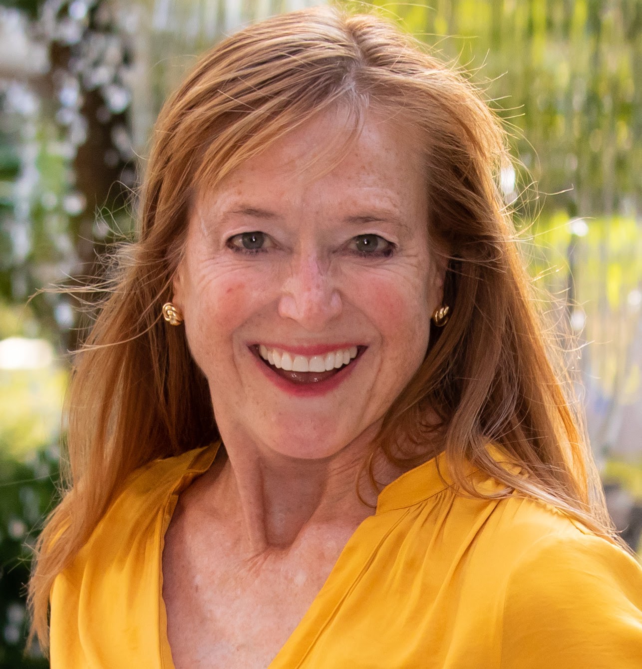 Red-headed white woman dressed in a yellow top faces the camera with a big smile
