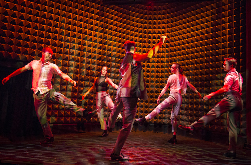 A group of dancers stand in a circle with their legs outstretched.