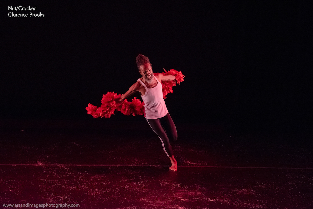 Black man, with hair in wrapped dreads, crowing his head  center stage runs with a red boa 