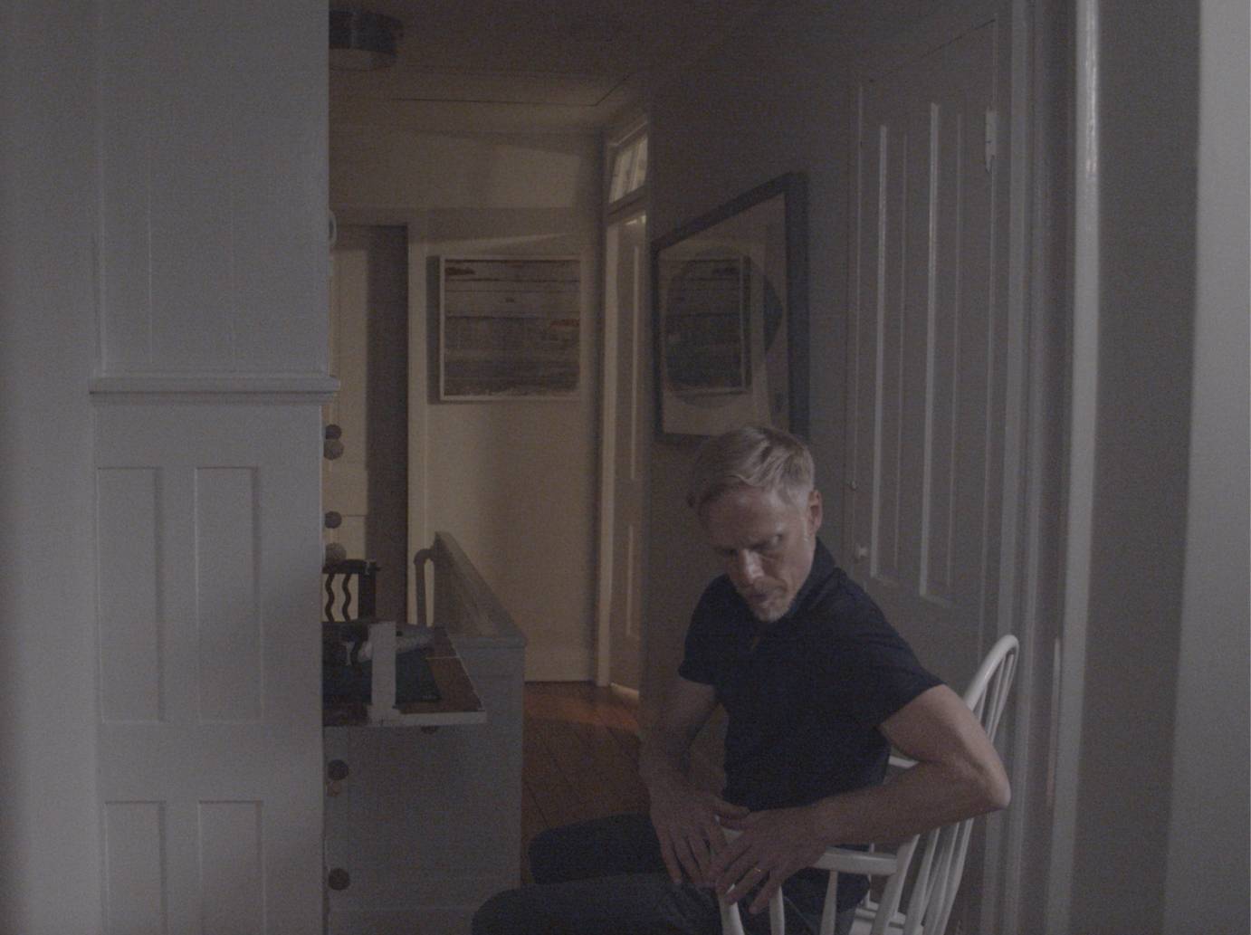 A man bends his arms at the elbows as he sits at a desk, a flight of stairs to his side