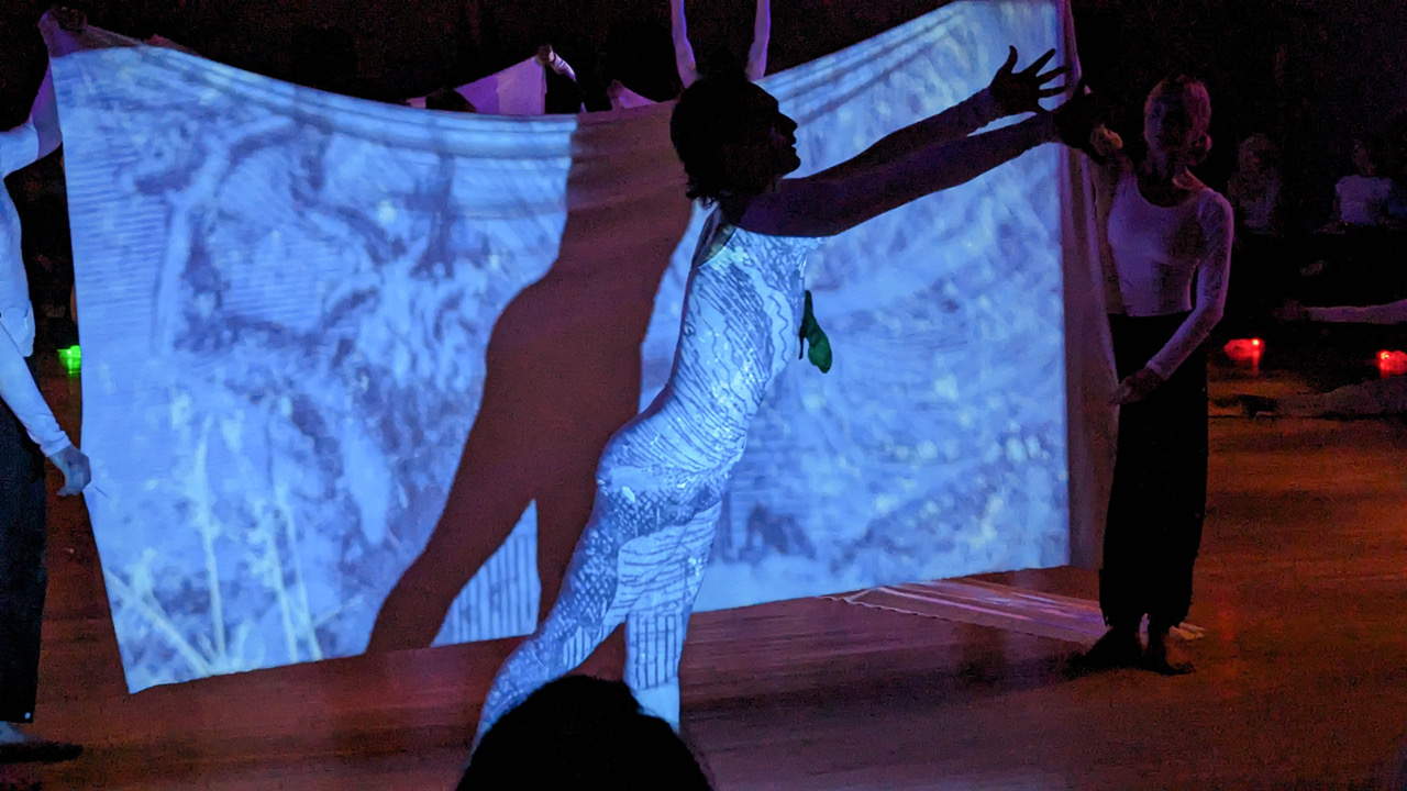 Projection of splotchy blue on a male body and the sheet behind. The dancer's shadow is seen on the sheet.