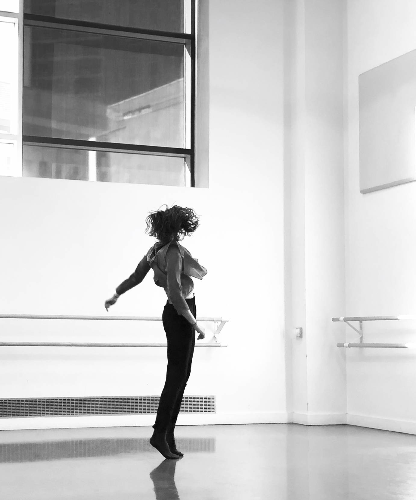 A black and white photo of a woman on her toes, her head and body turned away from the camera