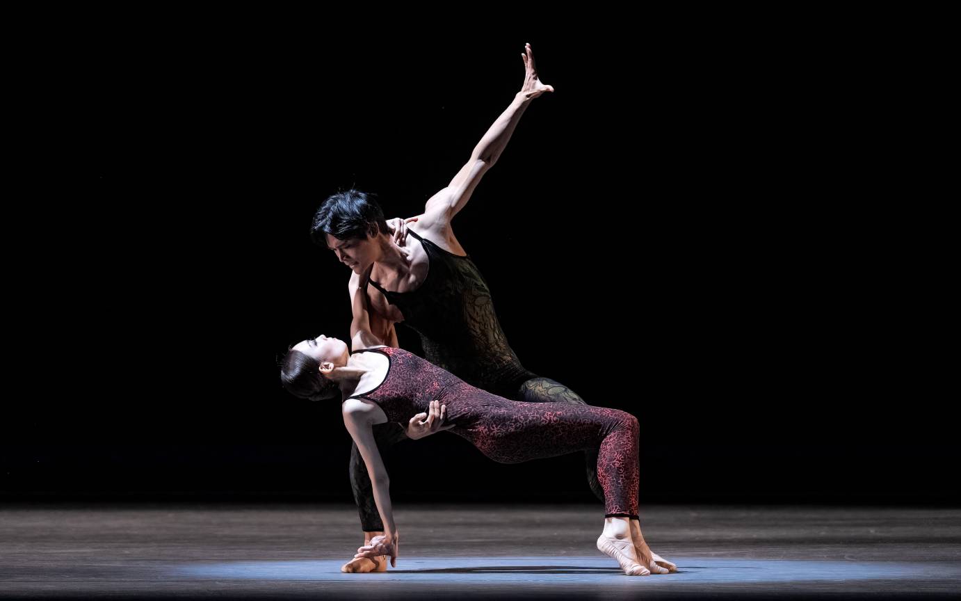 A woman slumps backward as a man holds her by the waist his other arm extended skyward. 