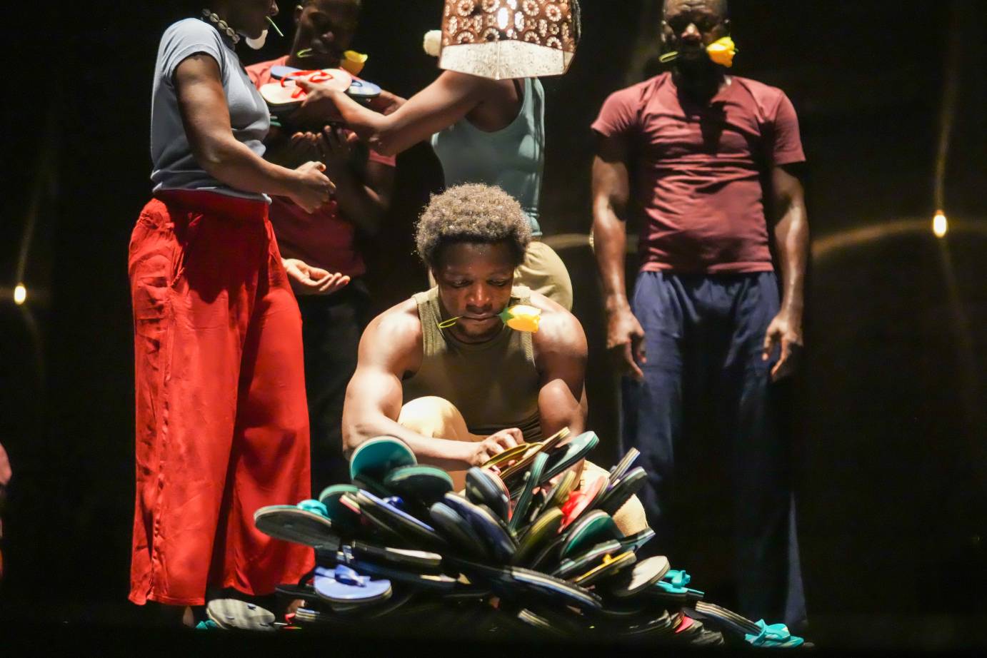 male dancer with flower in his mouth, kneeling before a pile of flip flops