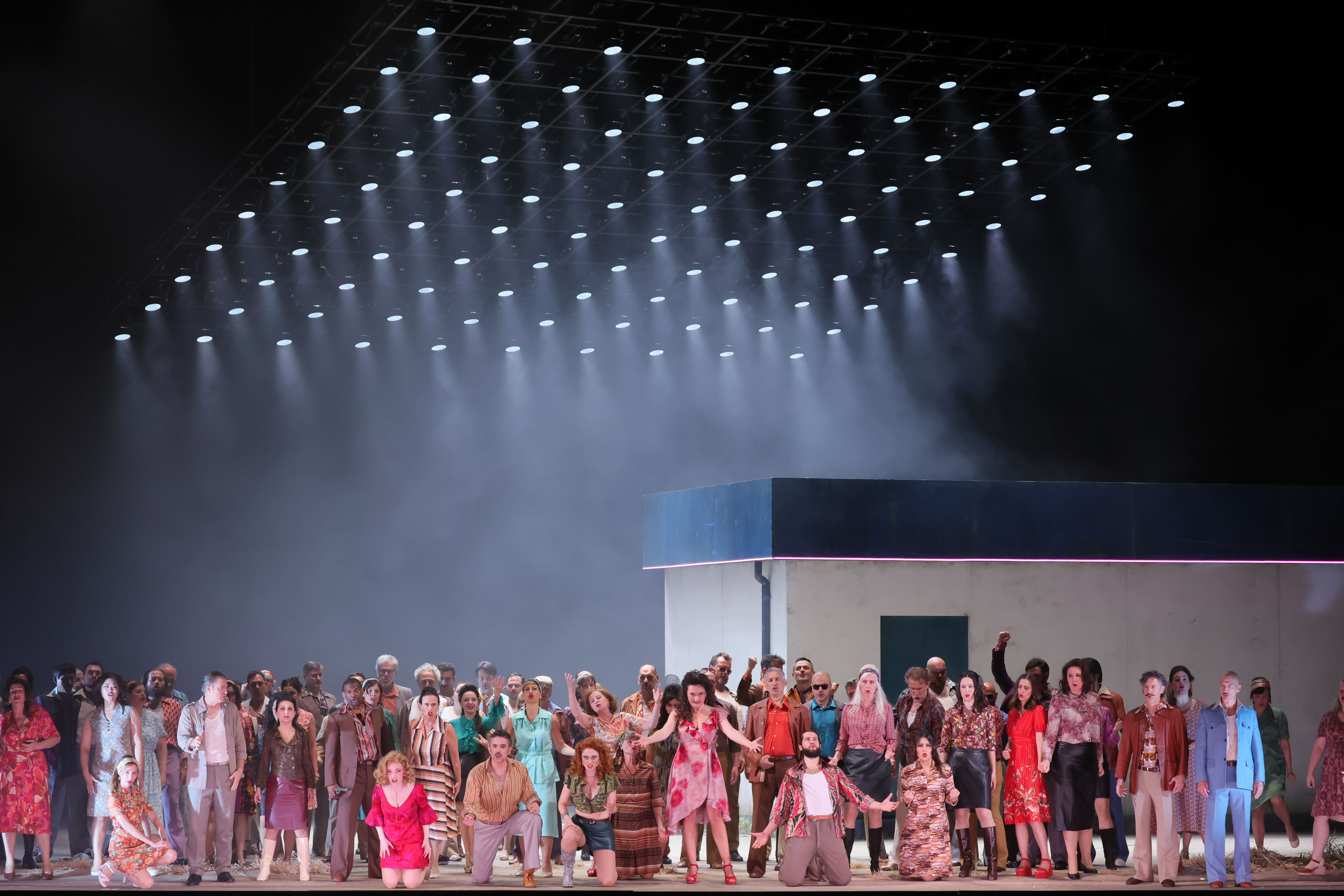 Carmen, center with arms flung wide, surrounded by the chorus