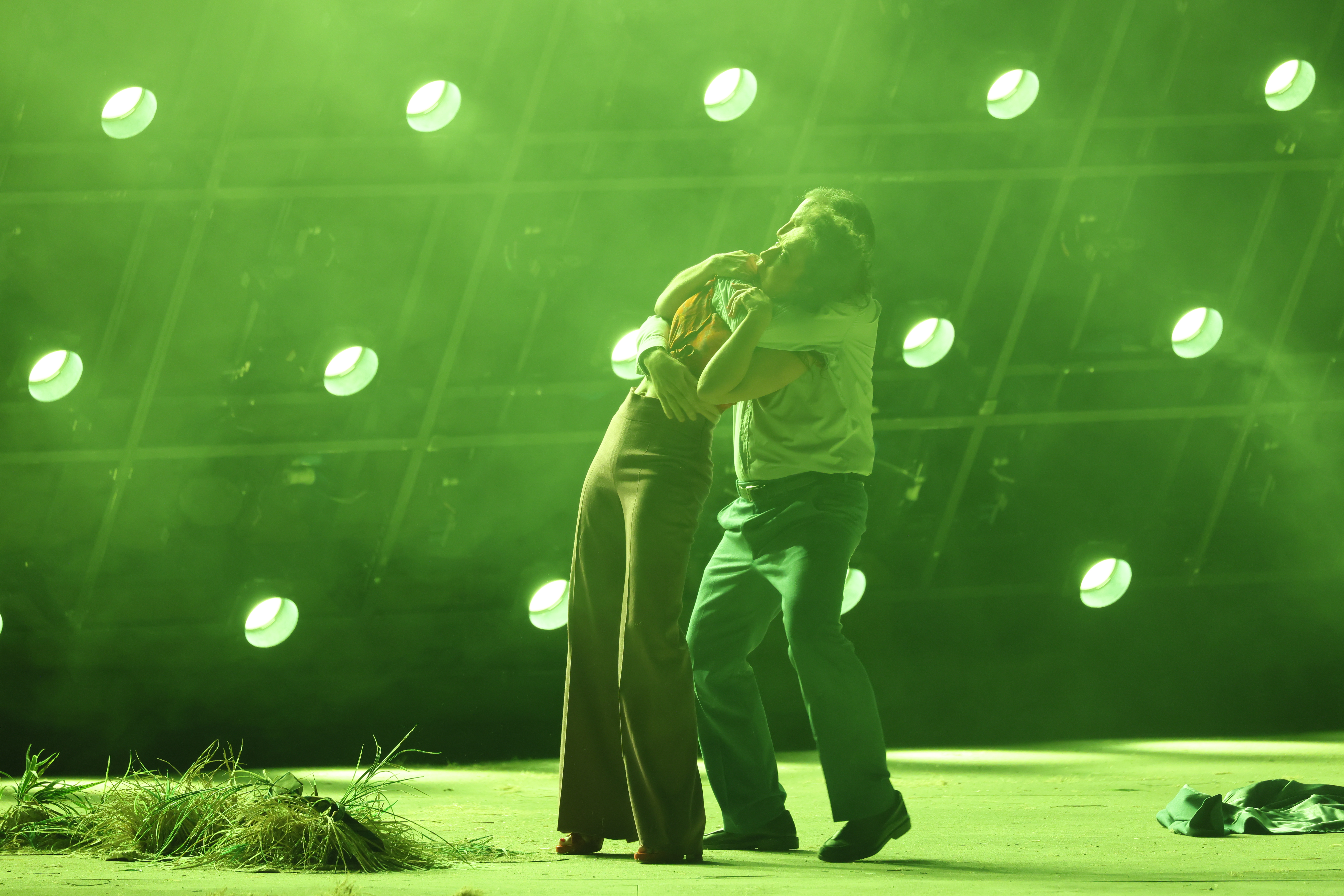 Washed in green light, Don José is wrapped around Carmen from behind amidst a struggle. 