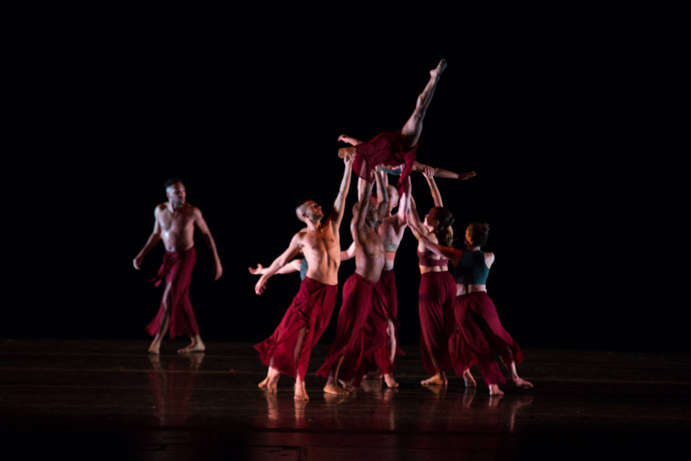 A group of red-clad dancers lift one woman in the air as a man looks on