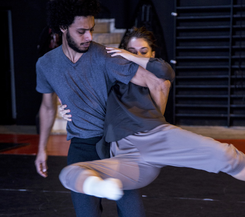 A close up of two dancers n rehearsal. The man picks up the female dancer. She leans on his hip and her legs are in a double attitude position in the air. She holds on to his shoulder and waist.