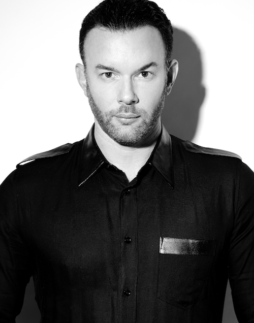 A headshot of Eryc Taylor in a black button up shirt. He stares directly into the camera.