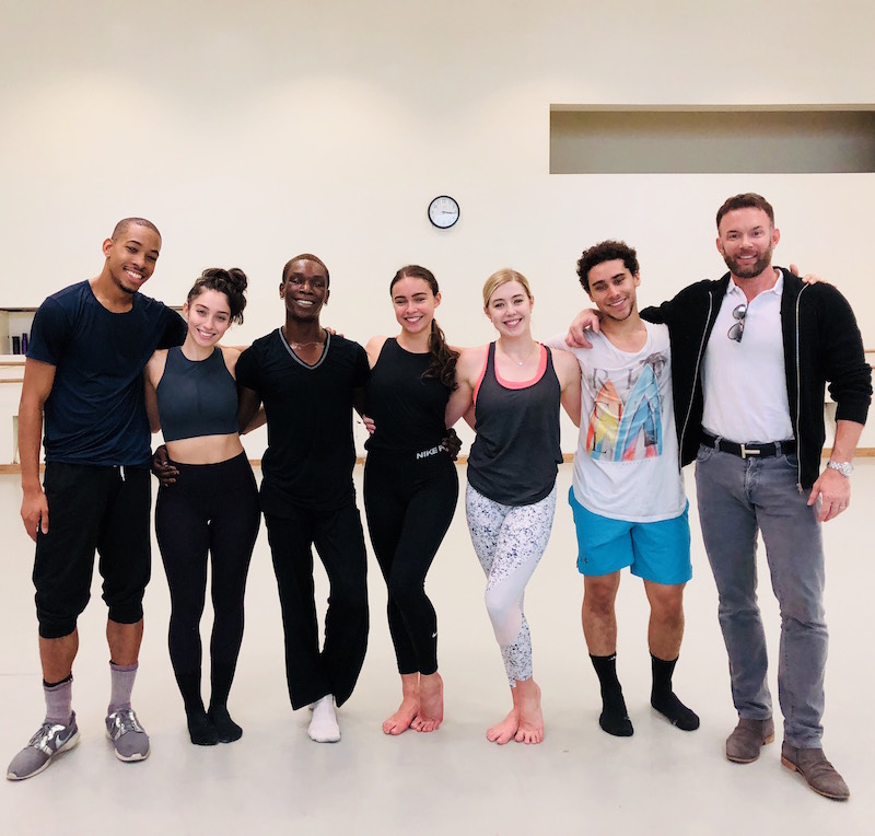 A group of dancers in practice clothes huddle up and pose for the camera