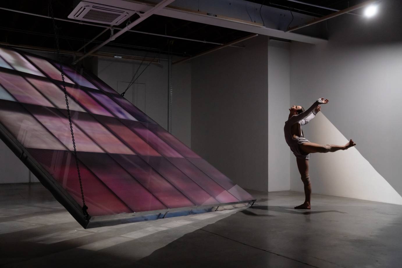 A dancer chest, head, and arms flung upward in back attitude in front of a garnet colored many paneled installation.