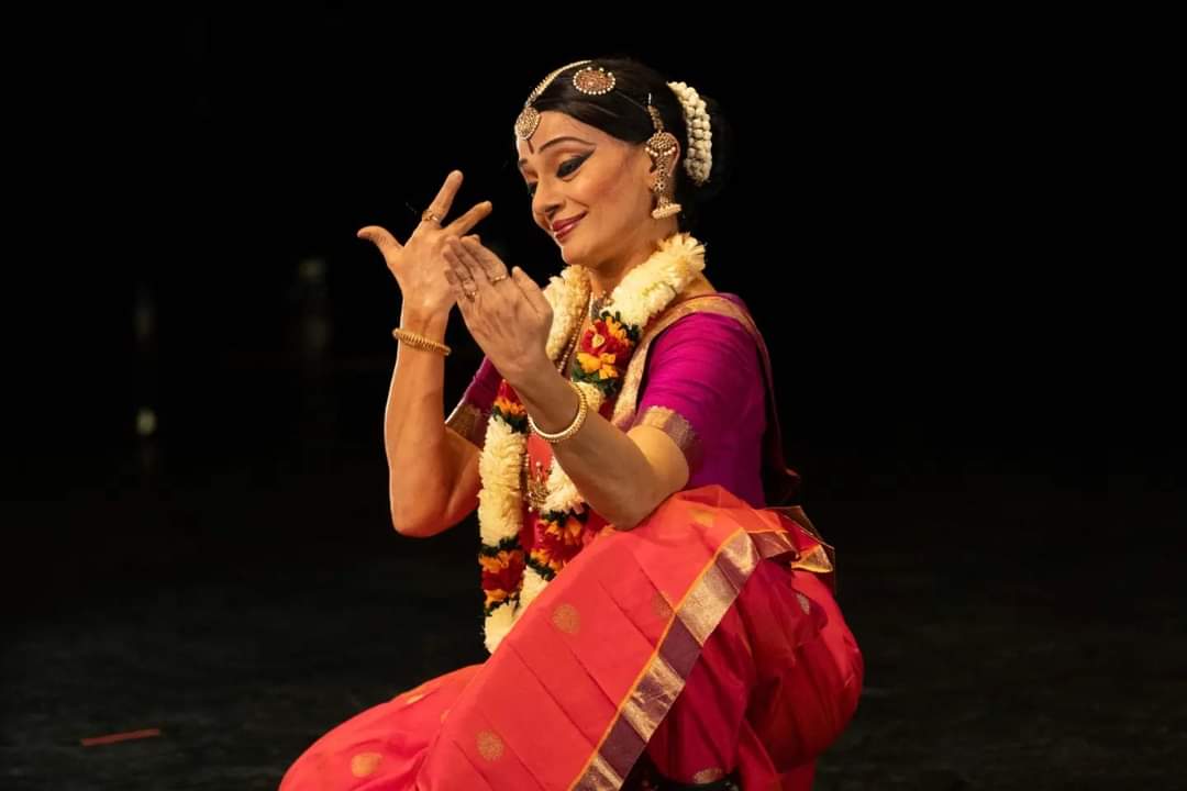 Malavika Sarukka caught in an expressive moment of hand gestures... beautifully made up and adorned she is radiant in a bright magenta and orange traditional outfit.