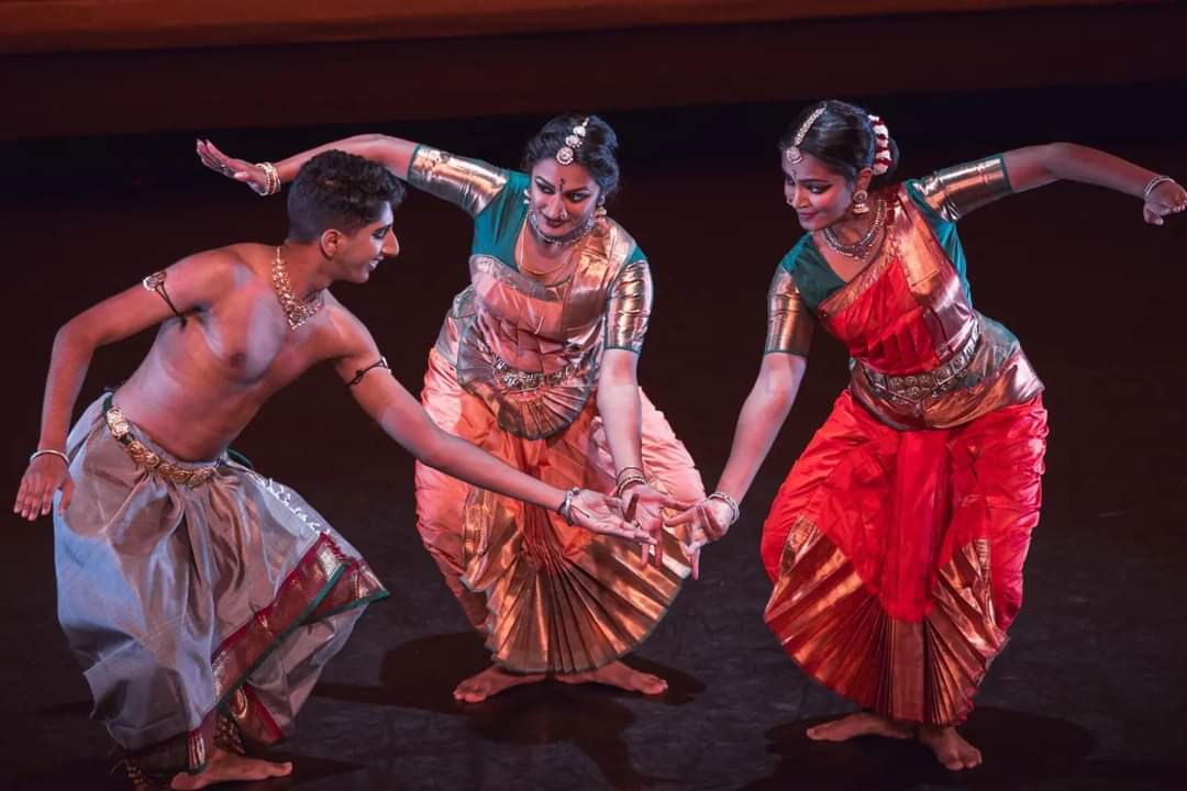 a group of three Indian dancers dressed in an array of colorful silks, jewels, and dark eye makeup.. play with each other as they enact a fable of a demon king and his demonesses.