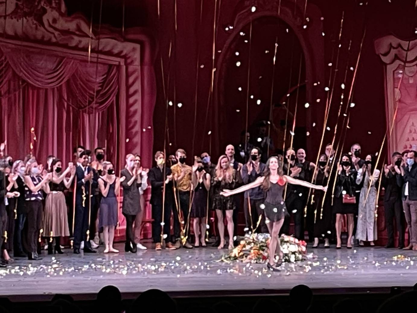 Maria Kowroski curtsies in a pile of flowers. Her coworkers stand behind her applauding.