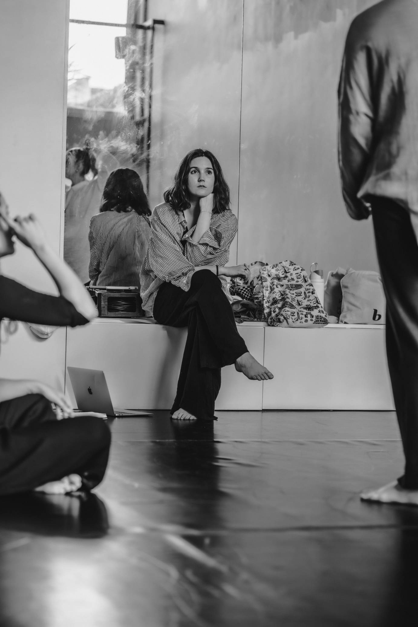 A black and white photo shows a seated women her back seen in a mirror, concentrating on what she sees before her.