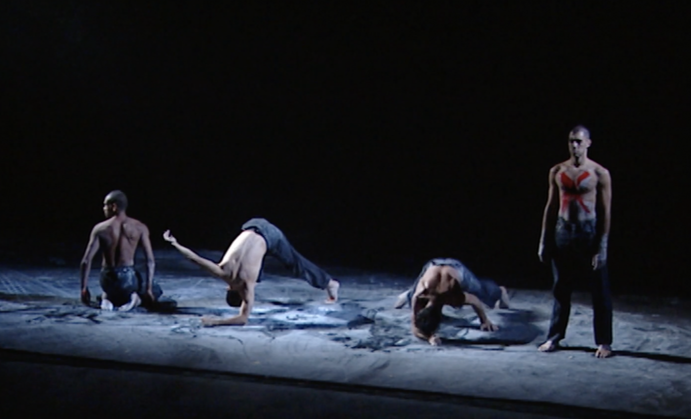 Four shirtless men stand in a row; one stares, another looks over his shoulder, ahead while the other two bend at the waist to touch the floor