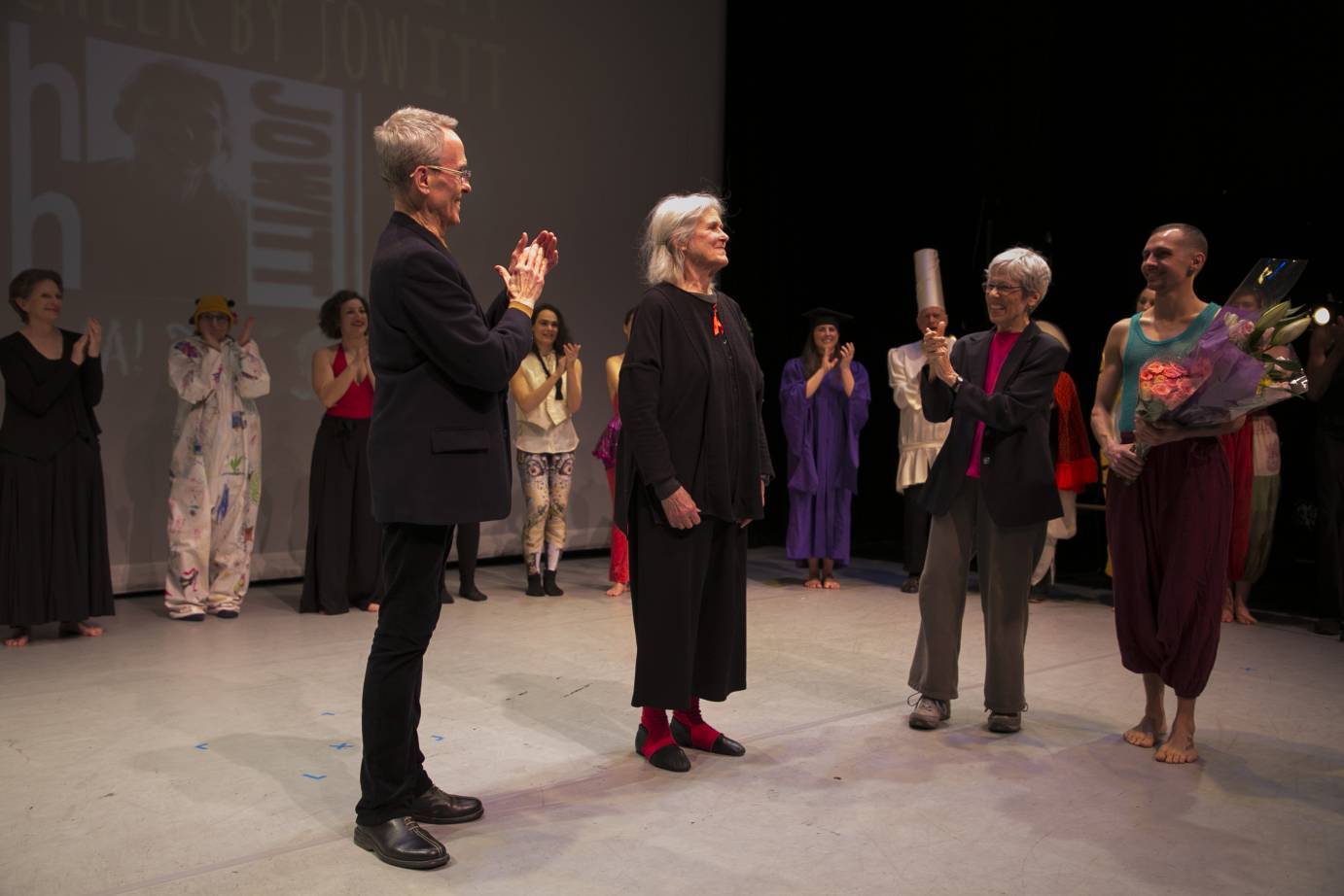 The performers surround Deborah as someone hands her flowers