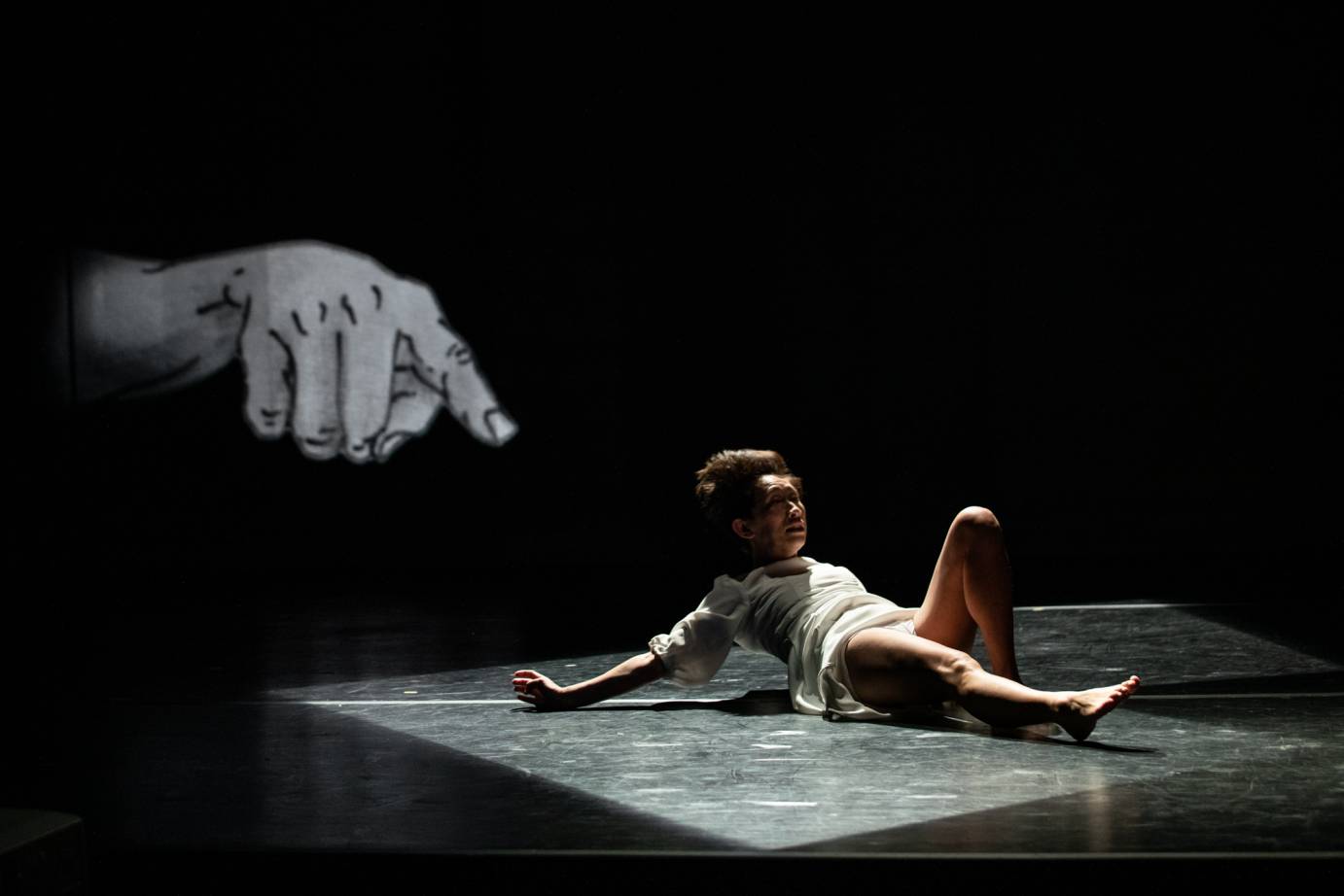 A woman lies on the ground as an illustration of a hand looms on a backdrop behind her