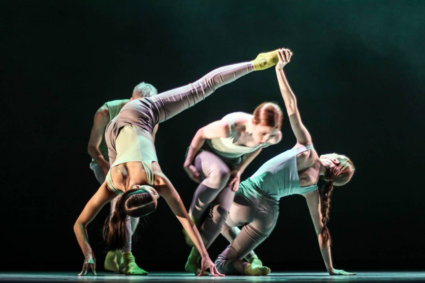 One dancer catches the foot of another dancer as two dancers run behind