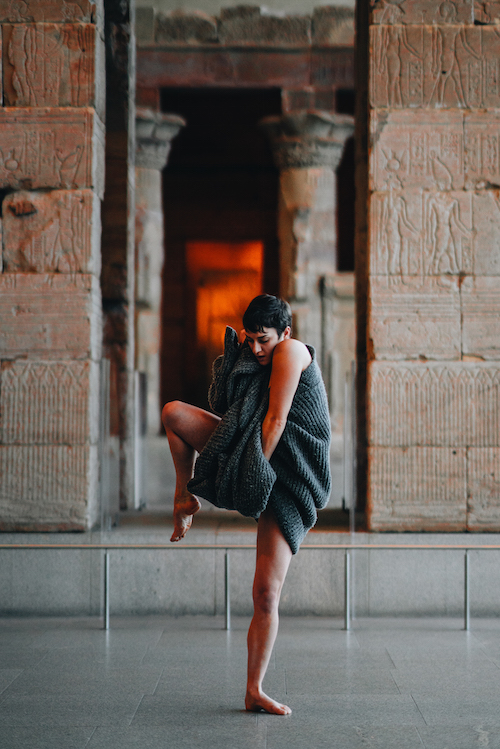 A dancer wraps a wool shaw around her. One foot is lifted in the air.
