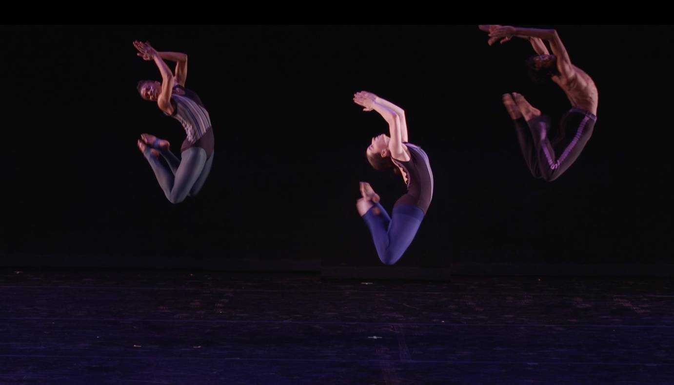 a trio of dancers spring into the air , their heads arching toward their toes, their arms uplifted in jubilation