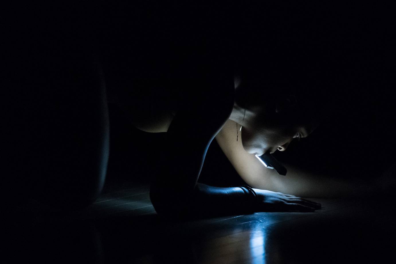 A woman with a flashlight in her mouth crawls on the floor