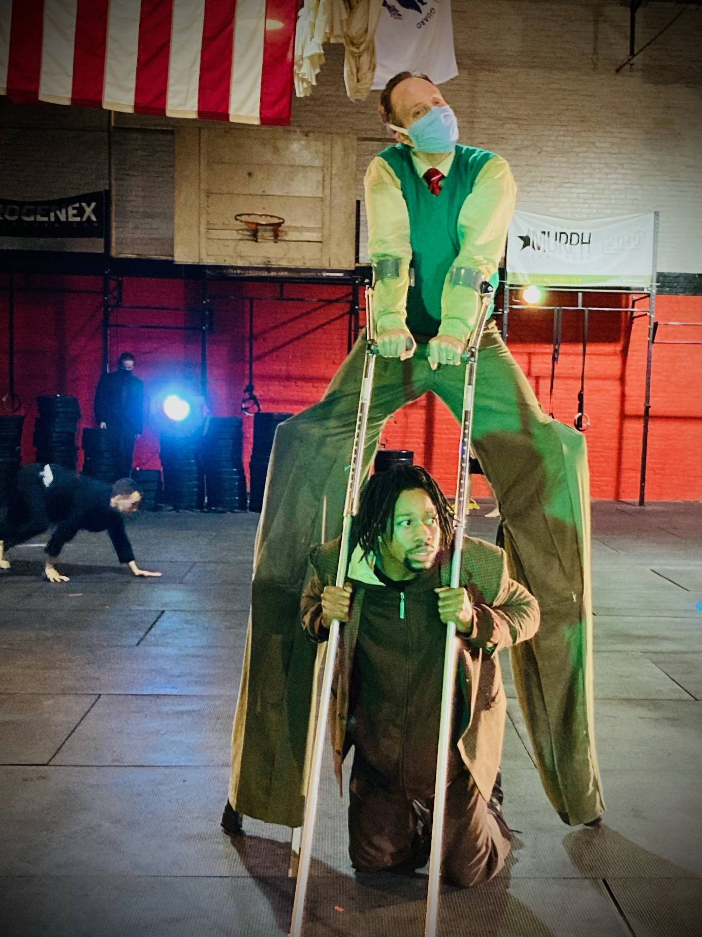 A man hides between the legs of a man in stilts