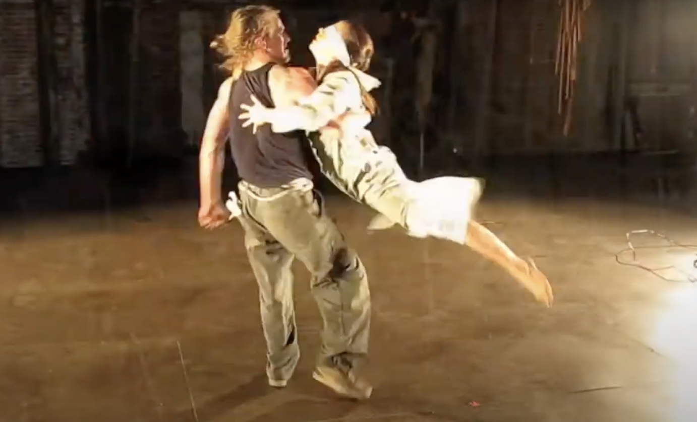 A shaggy-haired man lifts a blindfolded woman