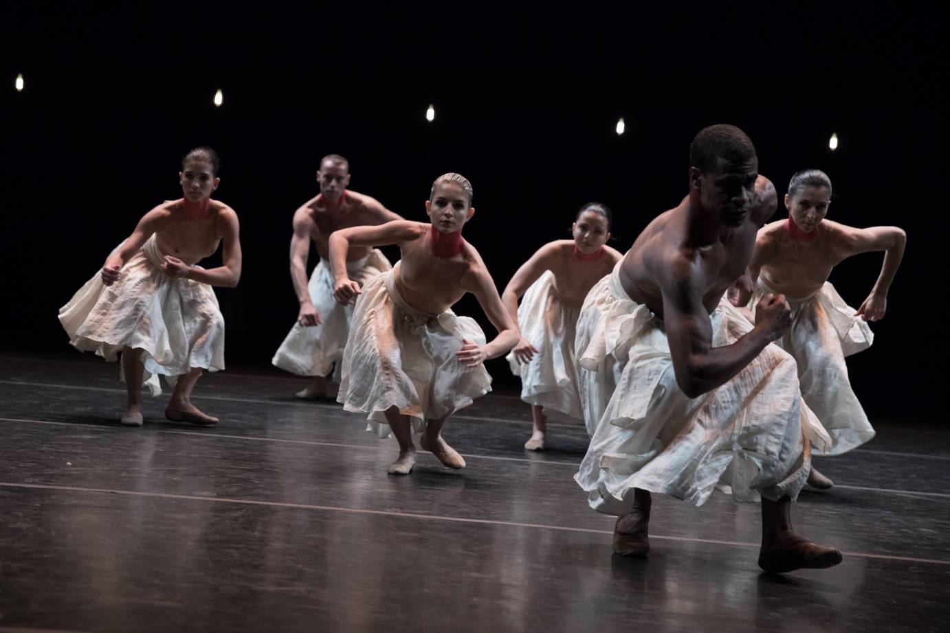 A large group of dancers walk with bent legs