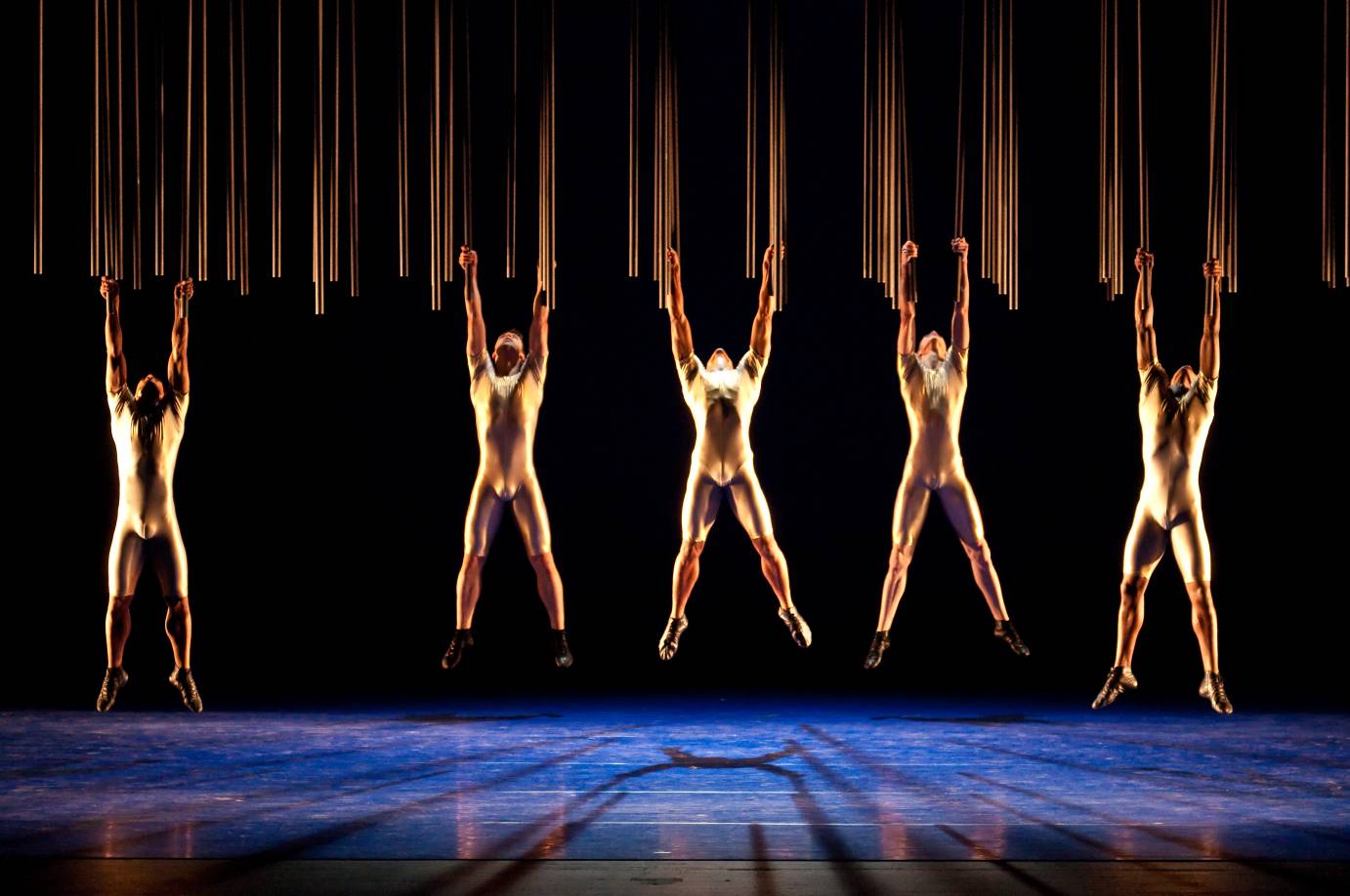 Three dancers hang from pipes