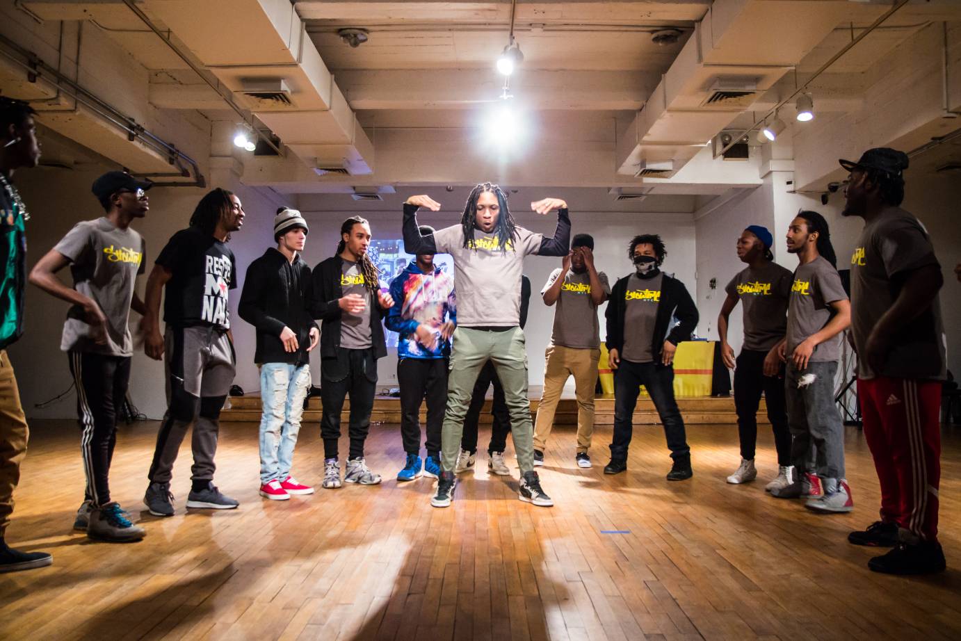 Men in t-shirts stand in a semicircle around another man who jumps in the air