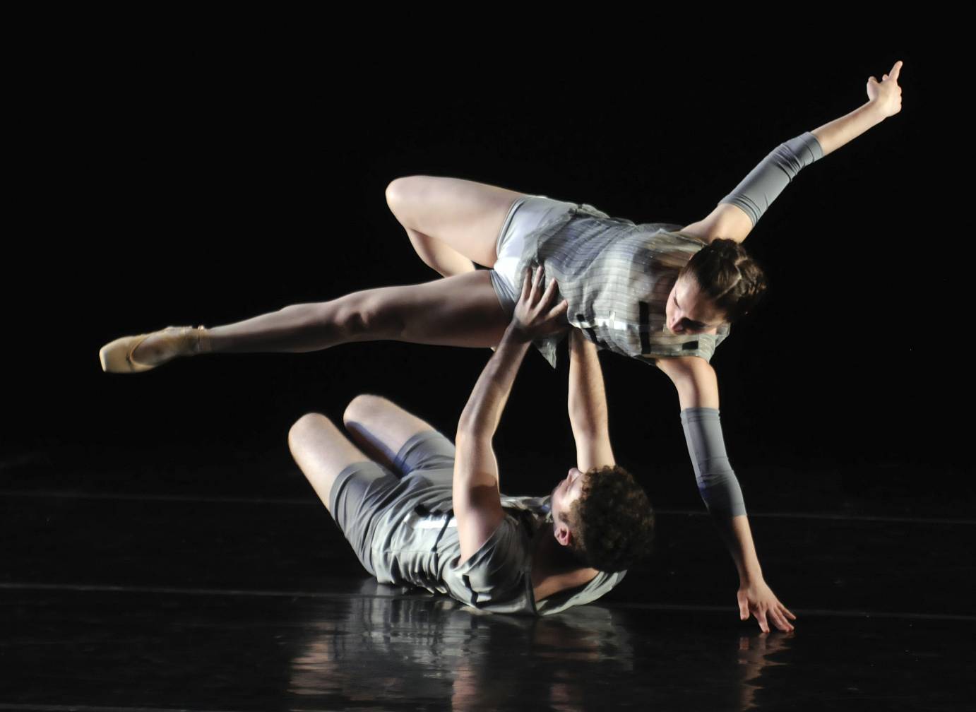 A man lying on the ground partners a woman in pointe shoes to leap over him