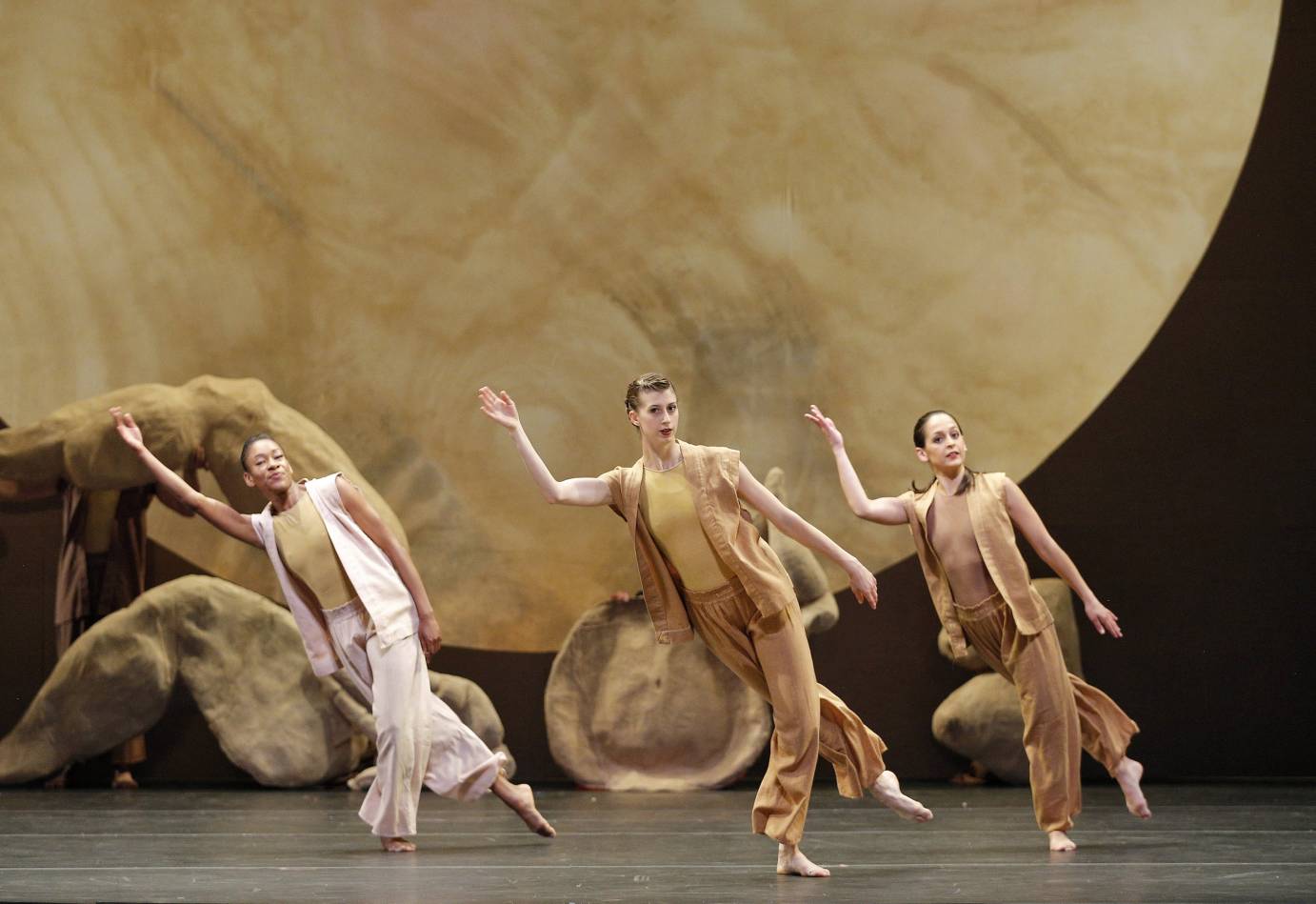 Three dancers gesture against a golden moon